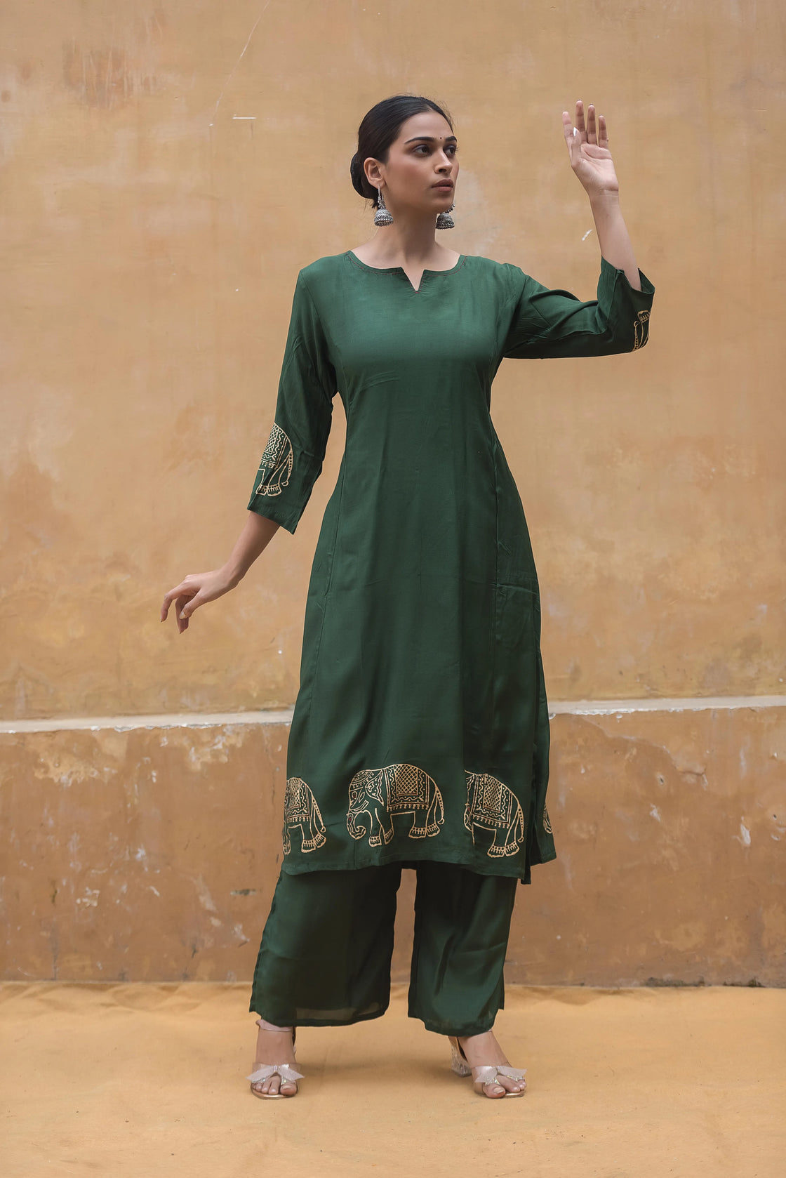 Woman in a bottle green muslin kurti pant set, hand raised to face, exuding a graceful and relaxed style.